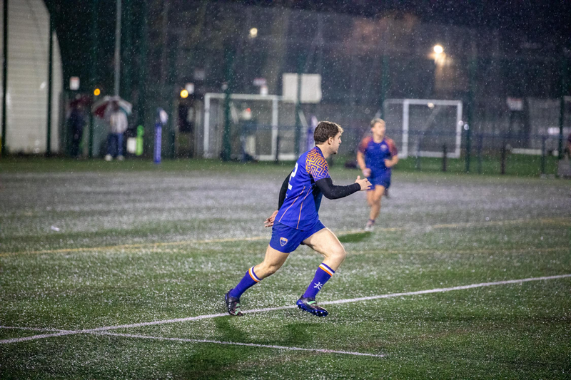 a rugby player running on a pitch while its raining