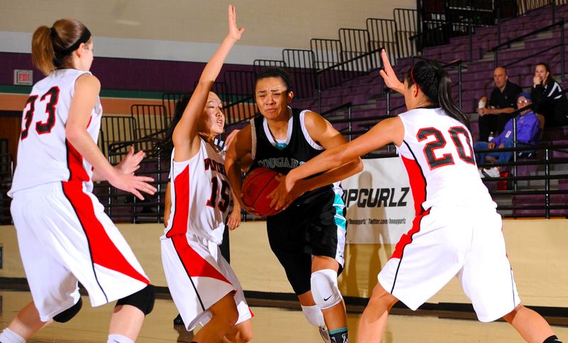 a female adult basketball player dribbling a basketball through three opposing team players
