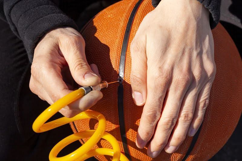 a man placing a ball pump needle into a basketball