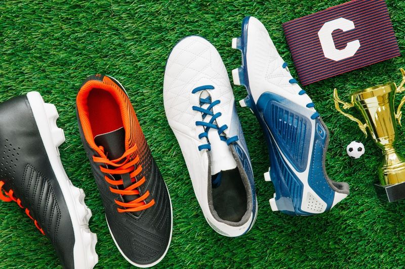 two pairs of soccer cleats on grass with a captain arm band and small trophy
