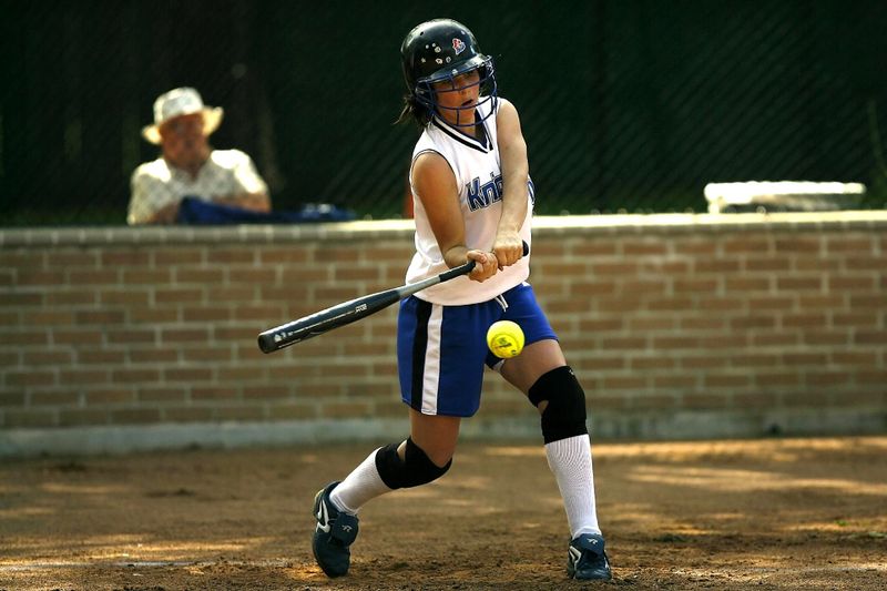 a youth softball player holding a steel softball bat about to hit a softball pitch