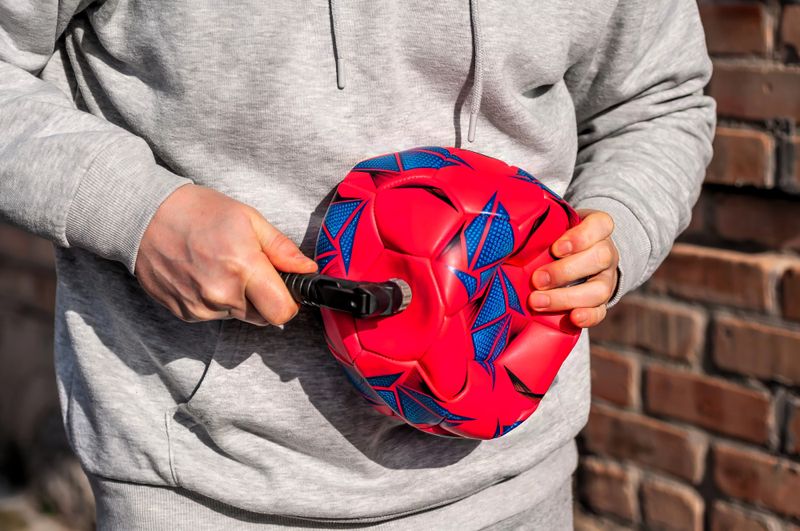a man deflating a red soccer ball using a ball pump and needle