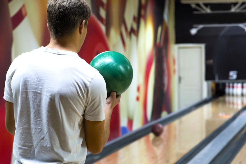 a male adult holding a green bowling bowl in his right hand