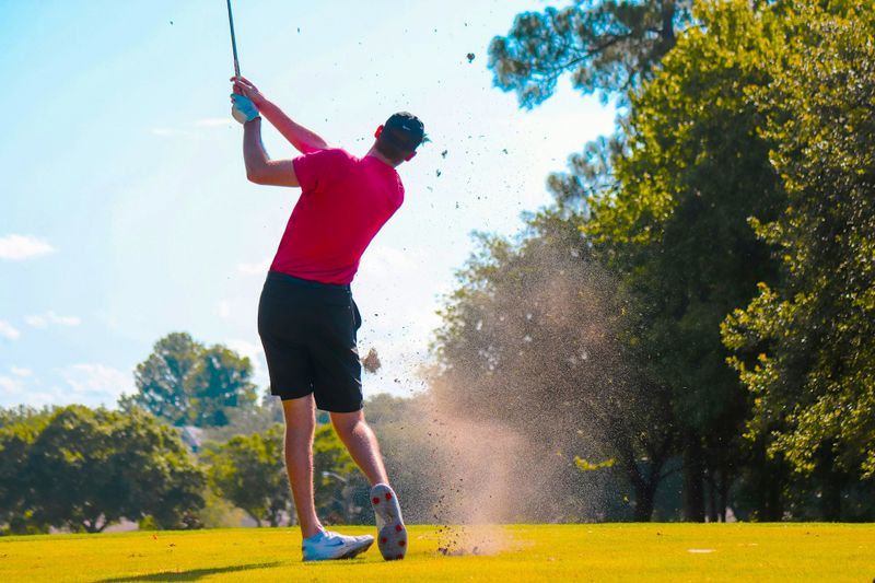an adult golfer hitting a golf ball with a cloud of mud in the air