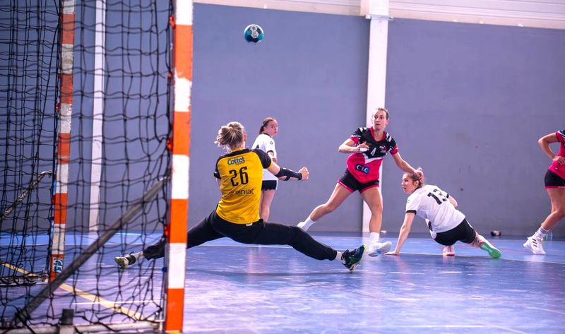 an adult female handball goalie reaching to block a shot