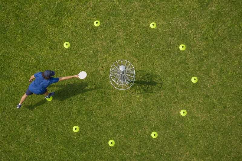 a male adult practicing putting disc golf at a basket in a circle