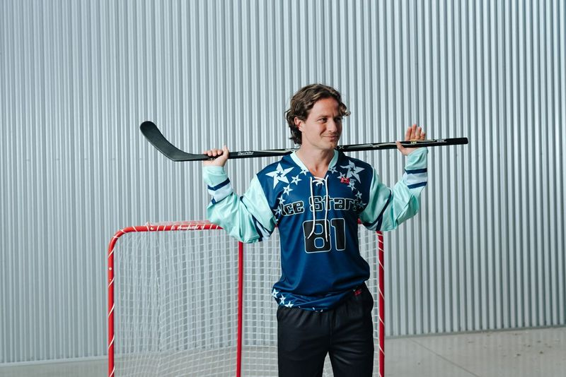 an adult male wearing a blue hockey jersey holding an ice hockey stick