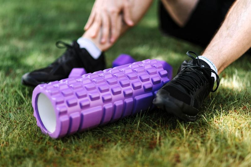a purple foam roller between an athletes feet on grass