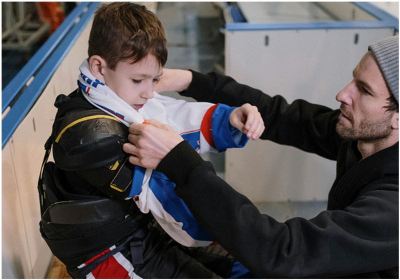 a father helping his child put on hockey gear