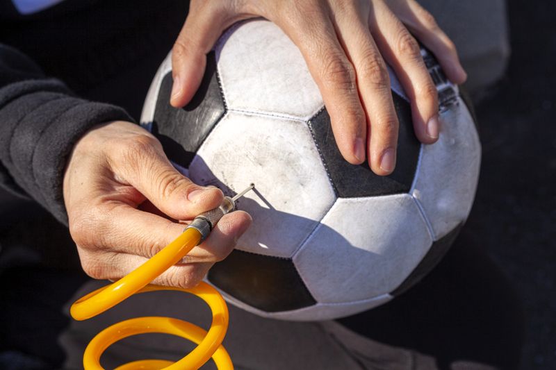 a person placing a inflation needle into a soccer ball