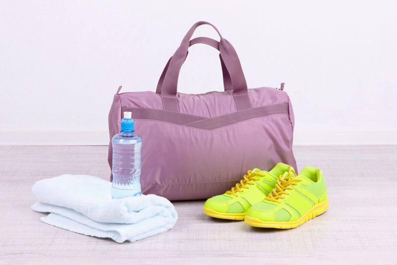 a purple gym bag with a towel, water bottle and gym shoes next to it