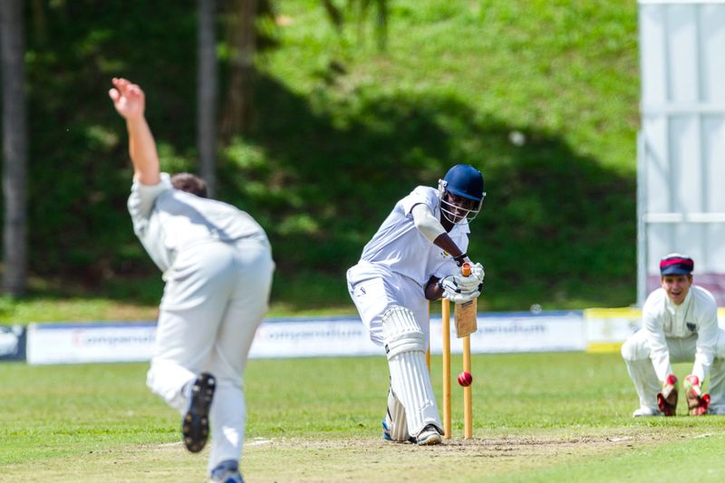 a youth batting a cricket ball to a cricket player