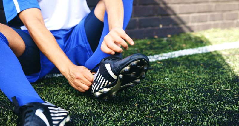 a young soccer player putting on a black soccer cleat