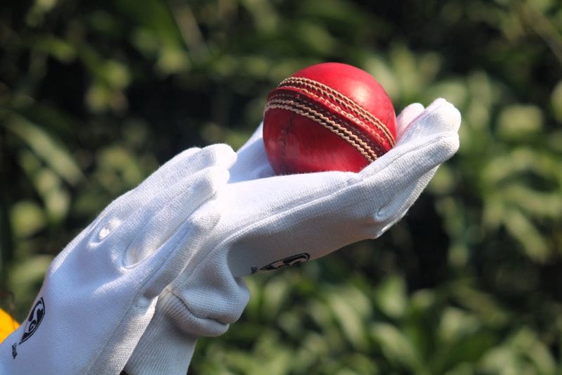 a person wearing white gloves holding a red cricket ball
