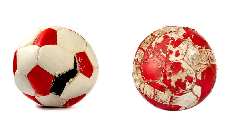two red and white soccer balls with rips and wear