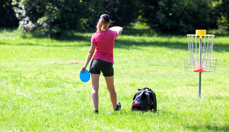 an adult female disc golf player practicing short throws on a disc golf basket