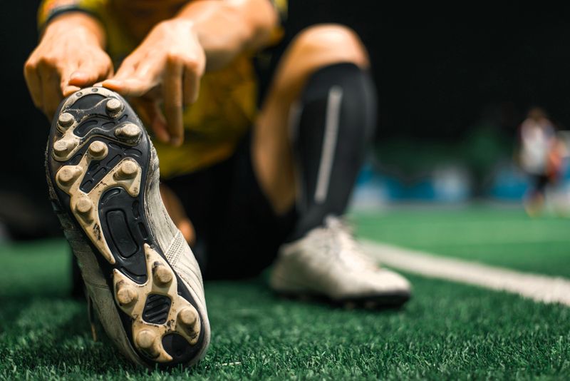 a soccer player wearing cleats stretching to his right foot