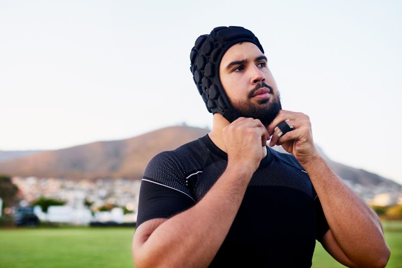 an adult male adjusting the strap on his rugby scrum cap