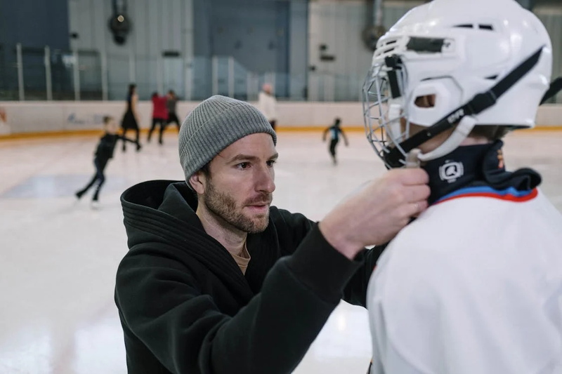 a coach helping a youth hockey player put on a helmet