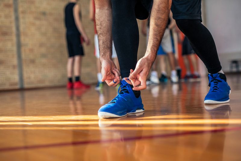 a male basketball player lacing up blue basketball shoes on a basketball court