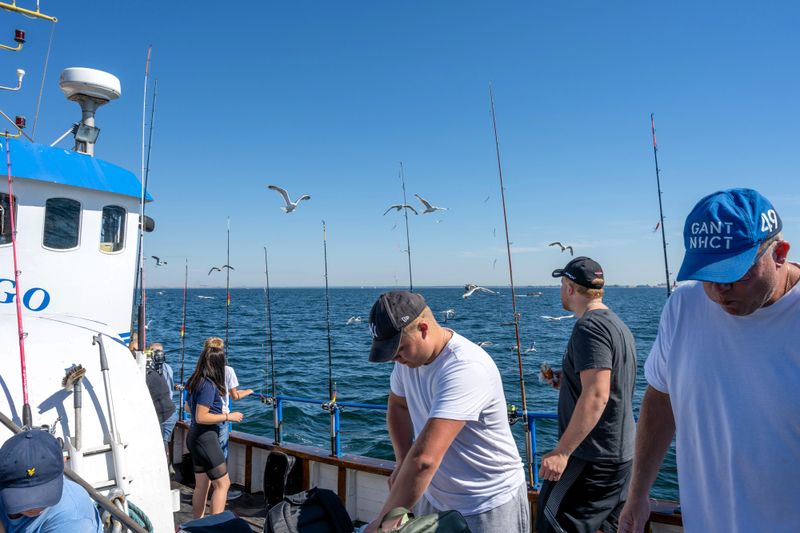 a group of people on a fishing boat with multiple fishing rods on the side of the boat