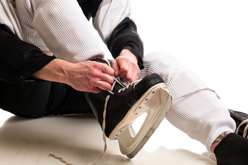 an adult male tying laces on his right ice hockey skate
