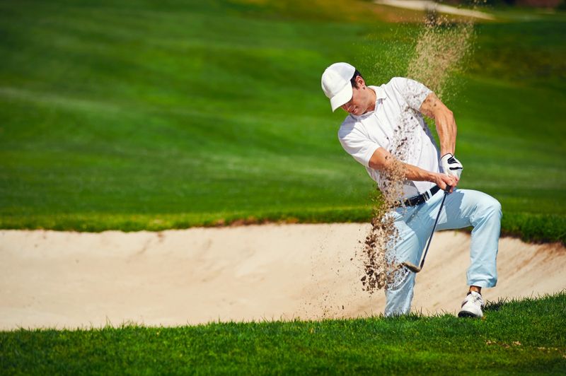 a male adult golfer hitting a golf ball out of a bunker
