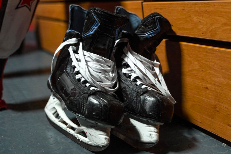 a pair of black hockey skates leaning against a wooden wall