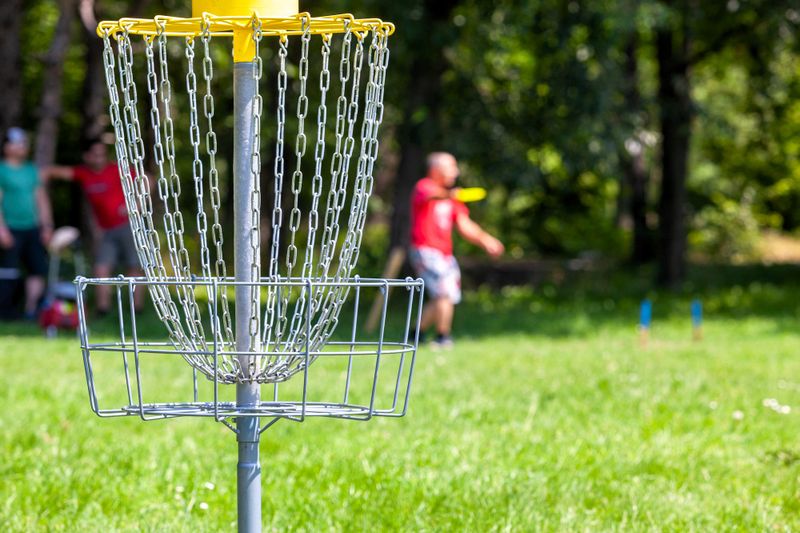 a yellow disc golf basket with a player throwing a disc from the background