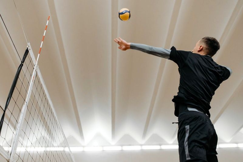 an adult man practicing his volleyball serve over a volleyball net