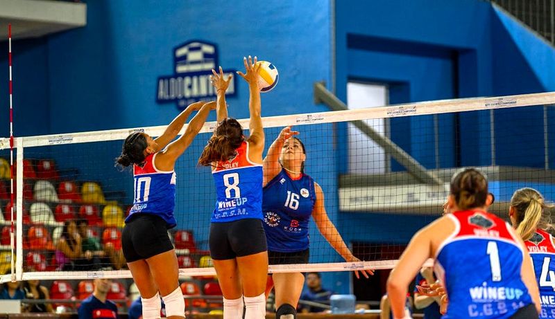 two volleyball players jumping to block the ball over a volleyball net