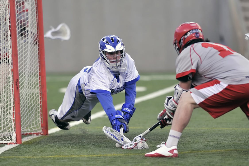 two lacrosse players in front of a goal post