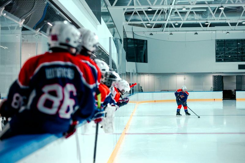 a youth hockey team leaning on a ice hockey rink wall waiting to get onto the ice rink