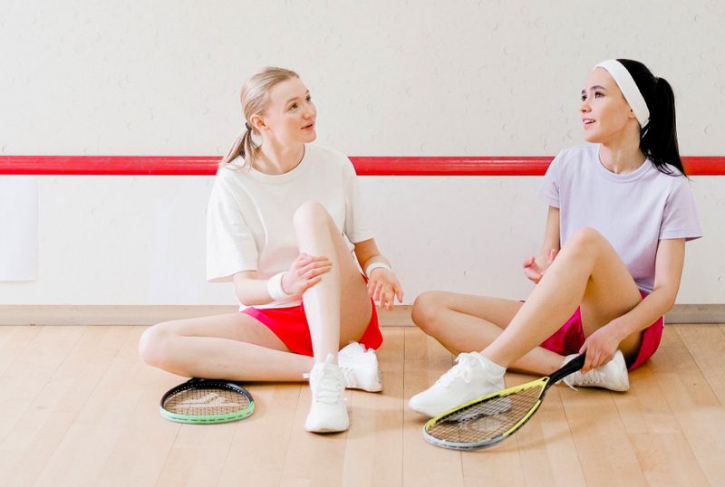 two female racquetball players sitting on a racquetball court having a conversation
