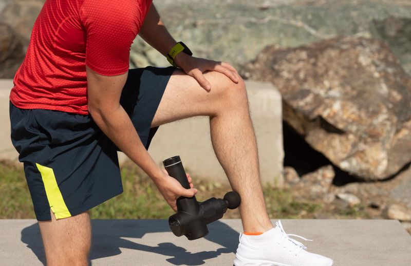 an adult man using a massage gun on his calf muscle