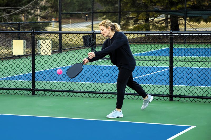 an adult woman about to serve a pickleball serve on an outdoor pickleball court