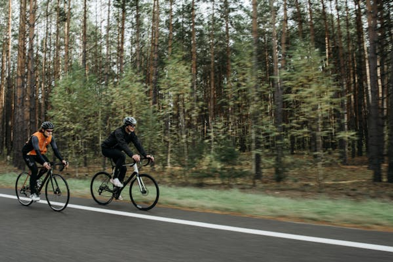 two cyclists cycling beside a wooded area