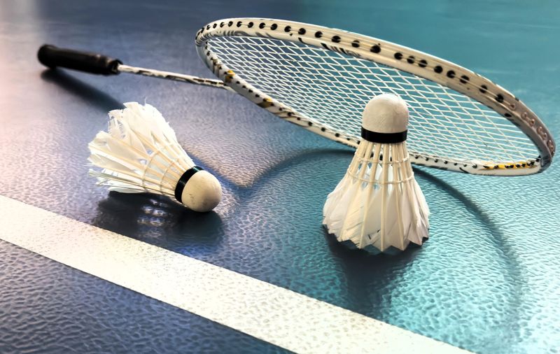 two shuttlecocks beside a badminton racket on a blue tennis court surface
