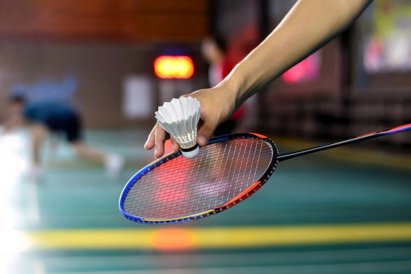 a hand placing a shuttlecock in front of a badminton racket