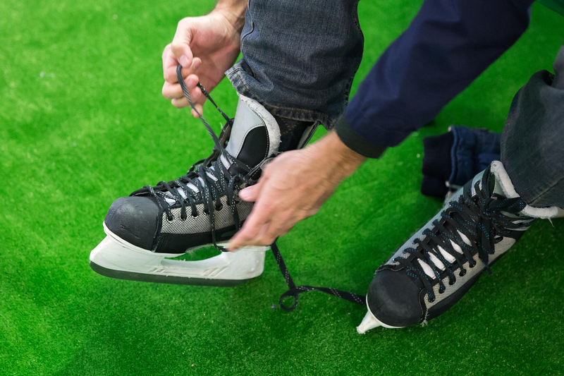 an adult male tying laces on a hockey skate on a green floor