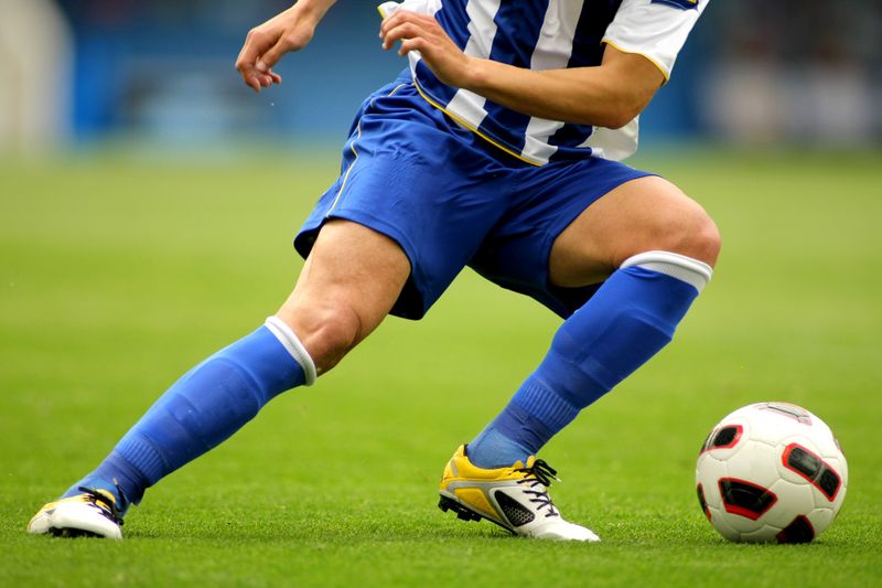 a soccer player wearing a blue and white soccer uniform leaning toward a soccer ball