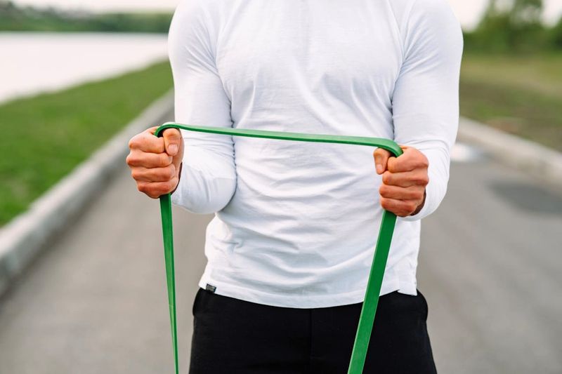 a man wearing a white shirt using a green resistance band