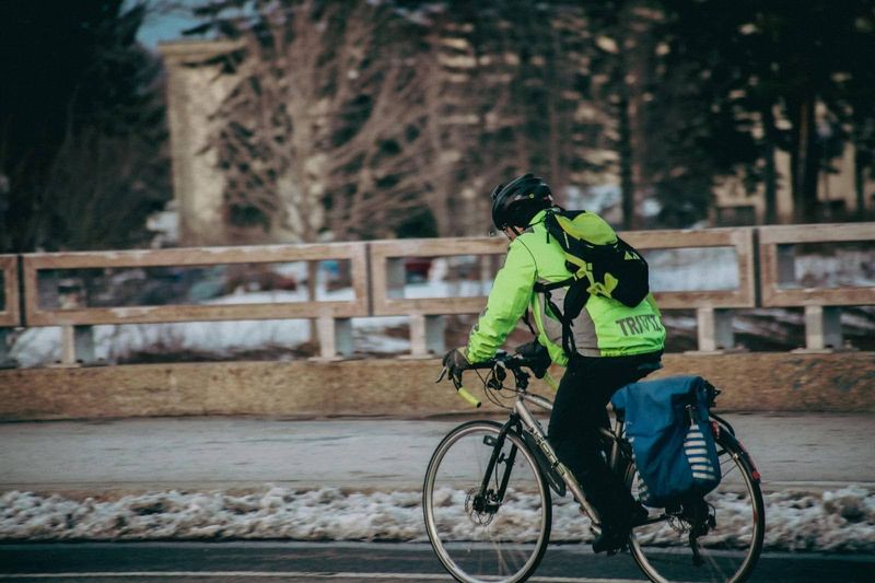 a cyclist cycling along a road next to a snowy sidewalk