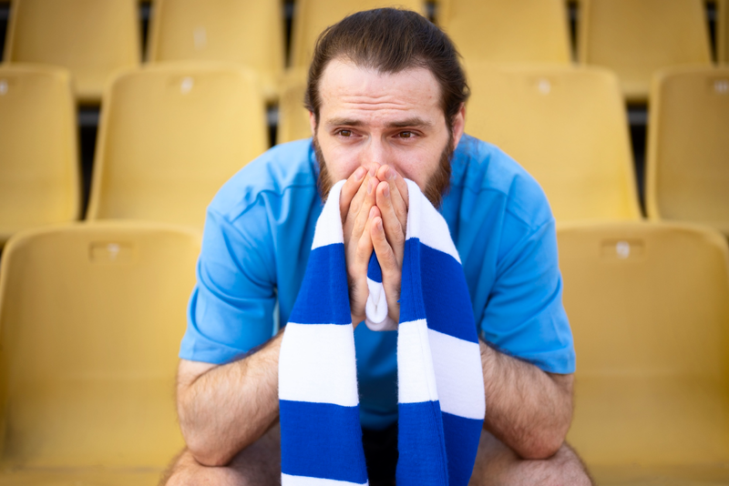 a disappointed soccer fan wearing a blue jersey and a blue and white scarf over his shoulder
