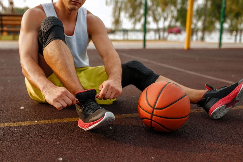 a man tying the laces on his basketball shoes sitting on a basketball court