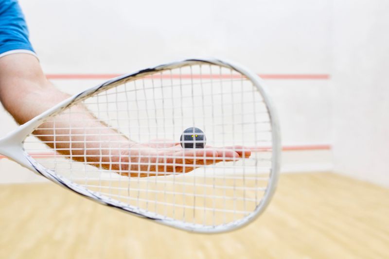 a racquetball racquet in front a hand holding a racquetball