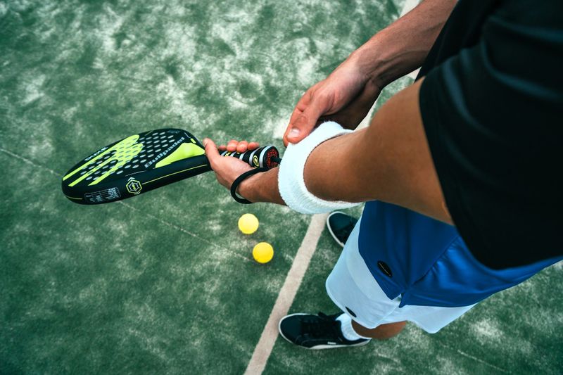 a padel player holding a padel racket adjutsing an arm sweatband