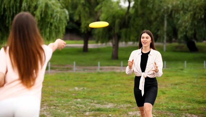 two adult females throwing a disc to each other outside