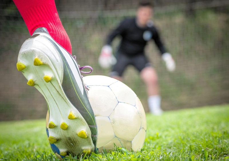 close up of a foot wearing a soccer cleat about to kick a soccer ball at a goalie