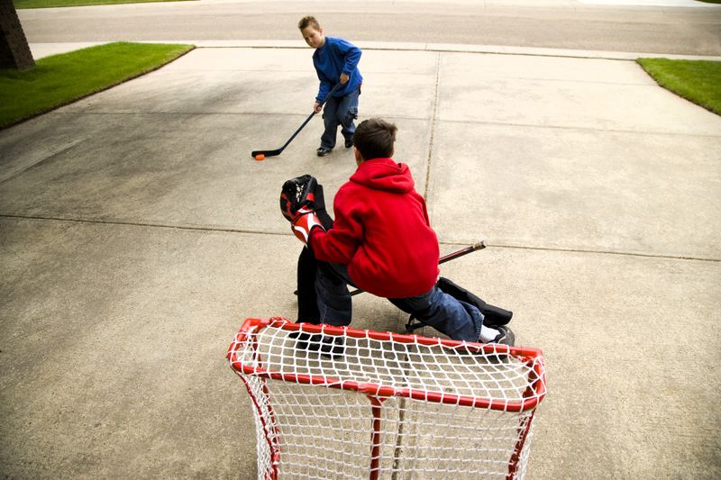 two youth boys playing with a mini hockey kit in their home driveway
